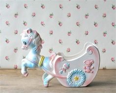 a toy horse pulling a baby carriage with teddy bears on it's back and pink flowers in the background