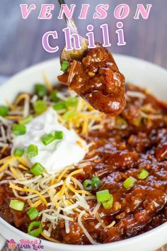 a spoon full of chili with cheese and sour cream on top is being lifted from the bowl