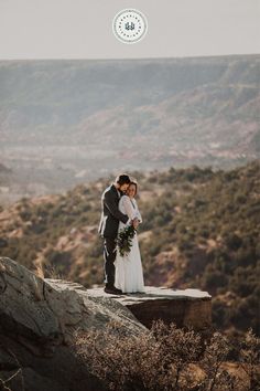 a bride and groom standing on top of a mountain