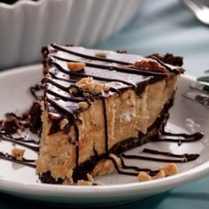 a piece of cheesecake on a white plate with chocolate drizzle and nuts