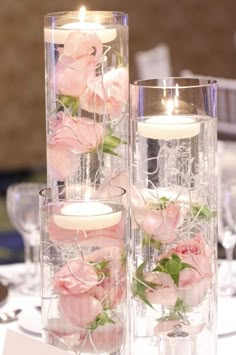 two clear vases filled with pink roses and candles