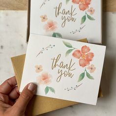 two thank you cards with watercolor flowers on them, one is gold and the other is pink