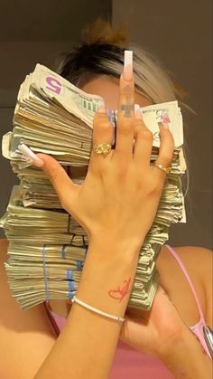 a woman covering her face with stacks of money in front of her head and fingers