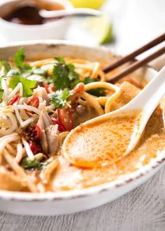 a white bowl filled with noodles, meat and veggies next to chopsticks