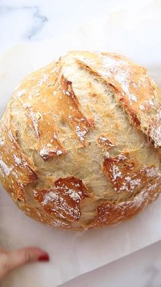 a loaf of bread sitting on top of a white counter next to a person's hand