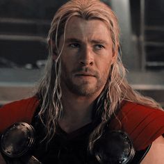 a man with long blonde hair wearing a red shirt and black leather gloves is looking at the camera