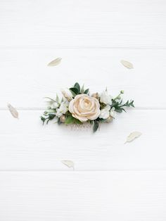 an arrangement of white flowers and greenery on a white wooden surface with leaves flying around