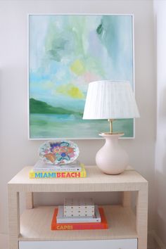 a table with a lamp, books and a painting on the wall in front of it