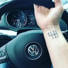 a person with a small tattoo on their wrist in a car, holding the steering wheel