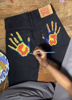 someone is painting their handprints on a pair of black jeans with paintbrushes