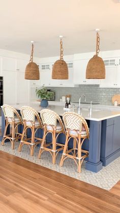 a large kitchen with blue island and wicker pendant lights hanging from it's ceiling