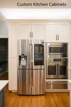 a stainless steel refrigerator and microwave in a kitchen with white cabinets, wood flooring and hardwood floors