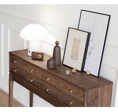 a wooden table topped with a lamp next to a framed painting and two pictures on top of it