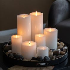 several white candles sitting on top of a black tray filled with rocks and pebbles in front of a chair