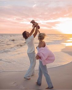 a man holding a baby up in the air while standing on top of a beach