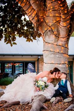 a bride and groom kissing under a tree in front of a building with lights on it