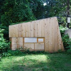 a wooden structure sitting in the middle of a lush green field next to a forest