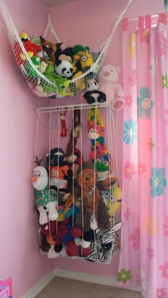 a room with pink walls and lots of stuffed animals on the shelves above it is a hammock filled with toys