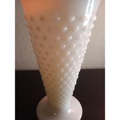 a white vase sitting on top of a table next to a black surface with dots all over it