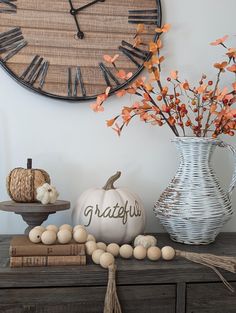 a white vase filled with orange flowers next to a clock and other decorations on top of a dresser