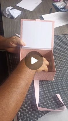 a person is holding a pink box with a white sheet in it and writing on the inside