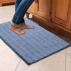 a person standing on a blue rug in the kitchen with their feet propped against the counter