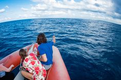 two people sitting on an inflatable raft looking out at the ocean while another person points