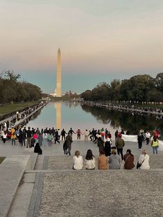 many people are gathered around the reflecting pool in front of the washington monument at sunset