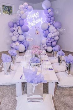 a table set up for a birthday party with purple balloons and silver vases on it