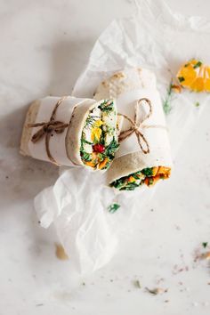 two wraps are wrapped in white paper and tied with twine on the top one is filled with vegetables