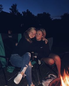 two women sitting next to each other in lawn chairs near a fire pit at night