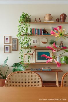 a dining room table and chairs with plants on the shelves above it, in front of a wall mounted bookshelf