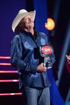 a man wearing a cowboy hat holding an award in front of a woman on stage