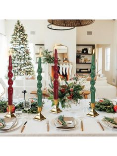 a dining room table set for christmas dinner with candles and greenery on the table