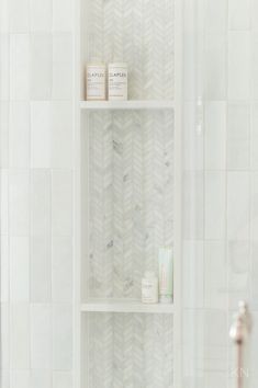 a bathroom with white tile and shelves in the shower area, along with two candles on top of each shelf