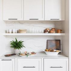 a kitchen with white cupboards and marble counter tops on both sides is filled with dishes