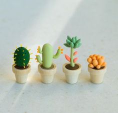 three small cactus plants in wooden pots on a white countertop, one is green and the other is orange