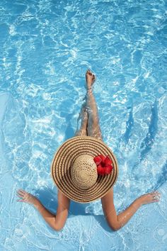 a woman wearing a straw hat floating in a pool with her feet up on the water