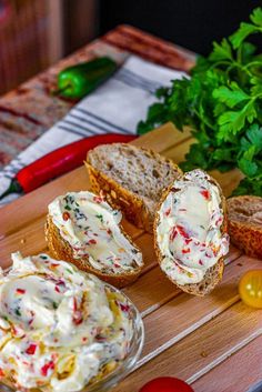 a wooden cutting board topped with bread and veggies next to other food items