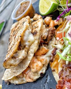 some tacos and other food on a slate platter with lime wedges next to it