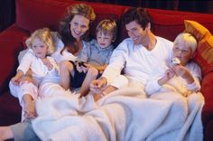 a family sitting on a red couch under a white blanket and smiling at the camera