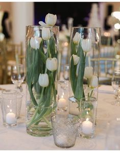 two vases filled with white tulips sitting on top of a table next to candles