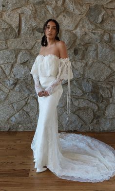 a woman in a white dress standing on a wooden floor next to a stone wall