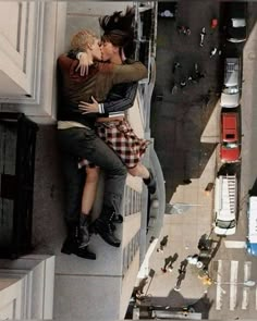 two people are kissing on the side of a building with cars and trucks in the background