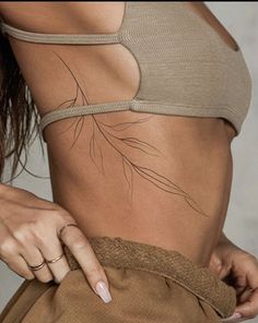 a woman is showing off her stomach with leaves on the bottom and side, while wearing a tan sports bra