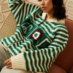 a woman sitting on a couch wearing a green and white sweater