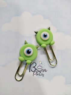 two green monsters with big blue eyes are sitting on paperclips in front of a sky background