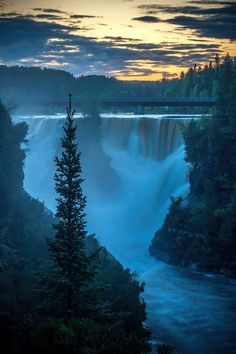 the sun is setting over a waterfall with water flowing down it's sides and trees on either side