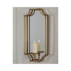 two candles are lit in front of a mirror on the wall with gold trimming