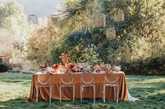 the table is set with orange cloths and flowers on it, along with chairs